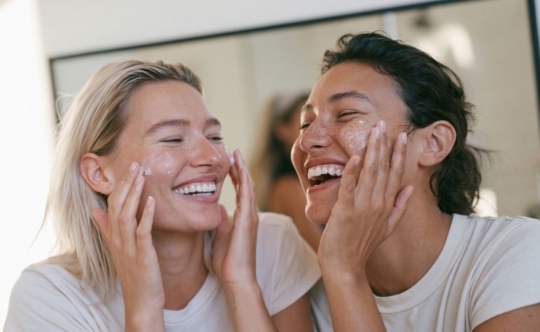 Two women of different ethnicities sharing a joyful skincare routine together, representing personalized skincare prescriptions tailored to every skin type