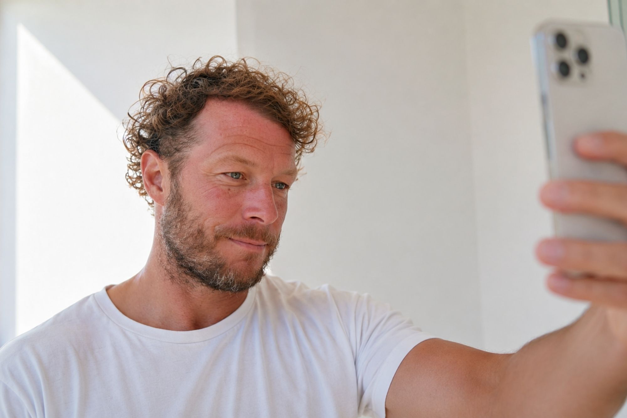 A man showing a receding hairline and thinning crown, takes a selfie on his phone for an online hair loss consultation
