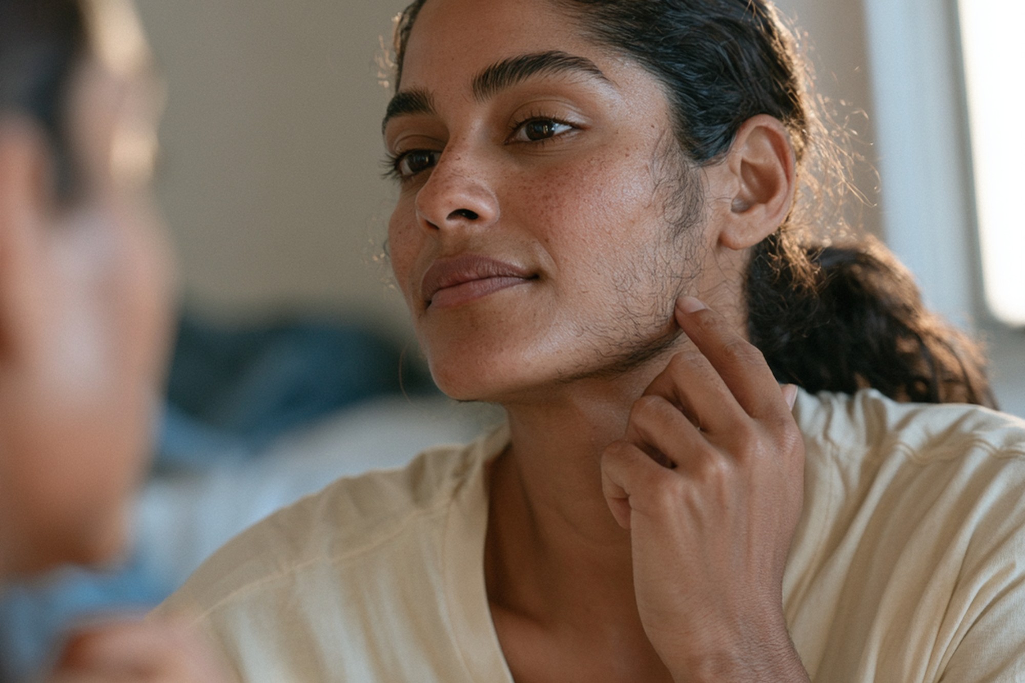 Hirsutism and facial hair in women Woman examining excess facial hair along her jawline in a mirror